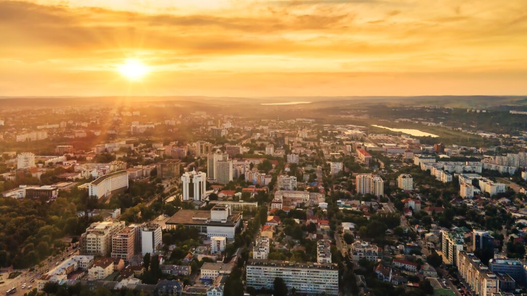 Aerial drone view of Chisinau downtown. Panorama view of multiple buildings, roads. Lush greenery, hills on the background, lakes. Sunset. Moldova